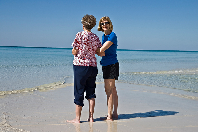 A caregiver and a senior woman standing on a beach