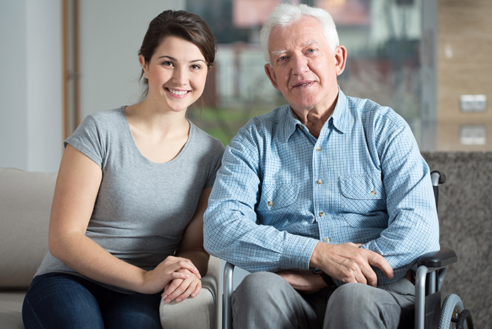 A smiling daughter sitting with her senior father, who is in a wheelchair