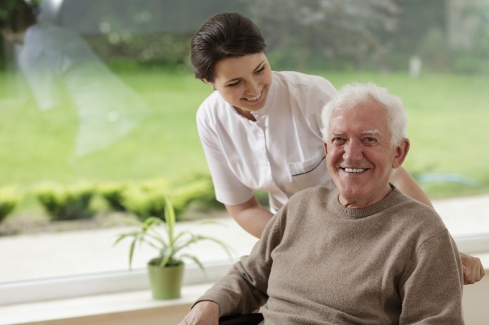 A smiling caregiver with her hands placed on the shoulder of a senior