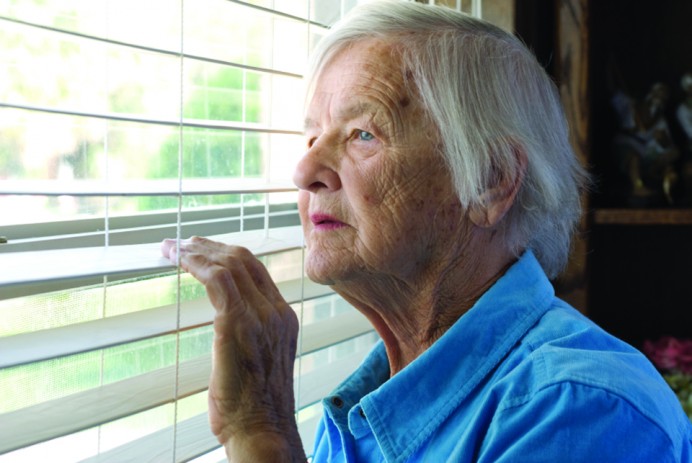 An elederly woman peers out a window