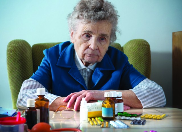 A frustrated senior sitting at a table full of prescription bottles