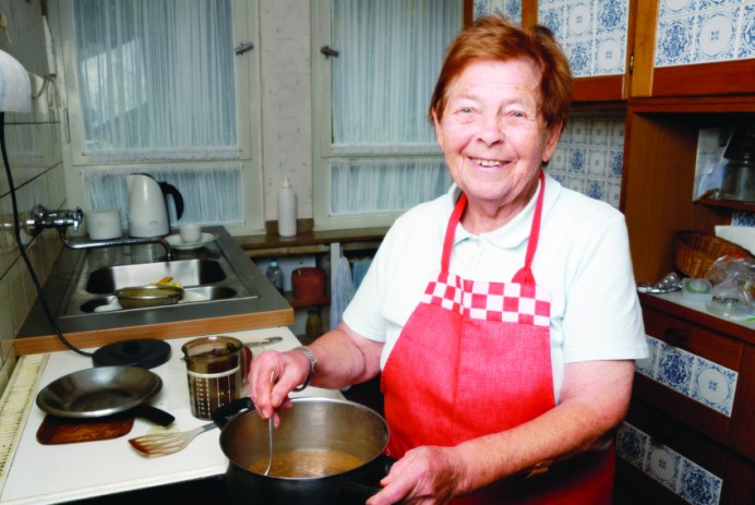 A smiling elderly woman cooking at a stove